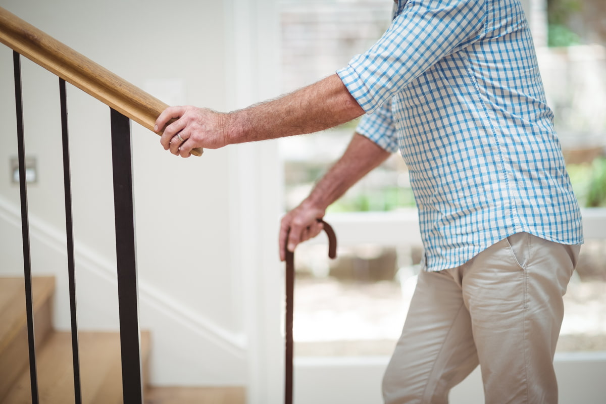 A person holds onto the handrail at the bottom of a staircase inside a house