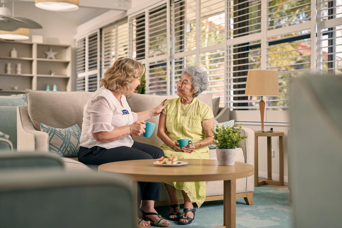 Resident sitting on lounge in community centre chatting with Aveo team member over tea16